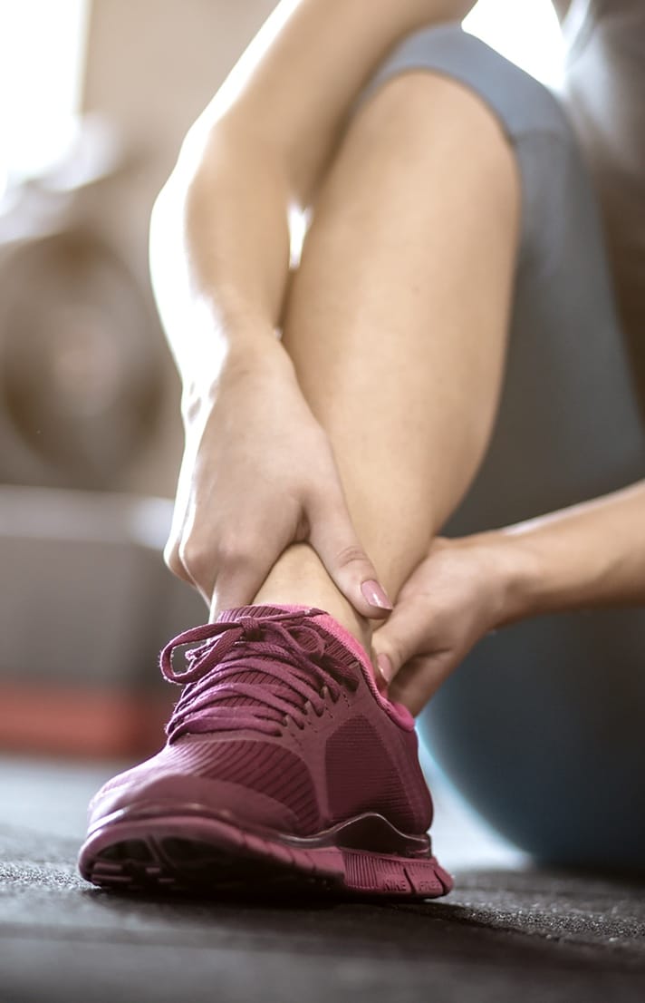 Woman's back wearing black sports bra with hand on shoulder Person grabbing their ankle wearing red running shoes