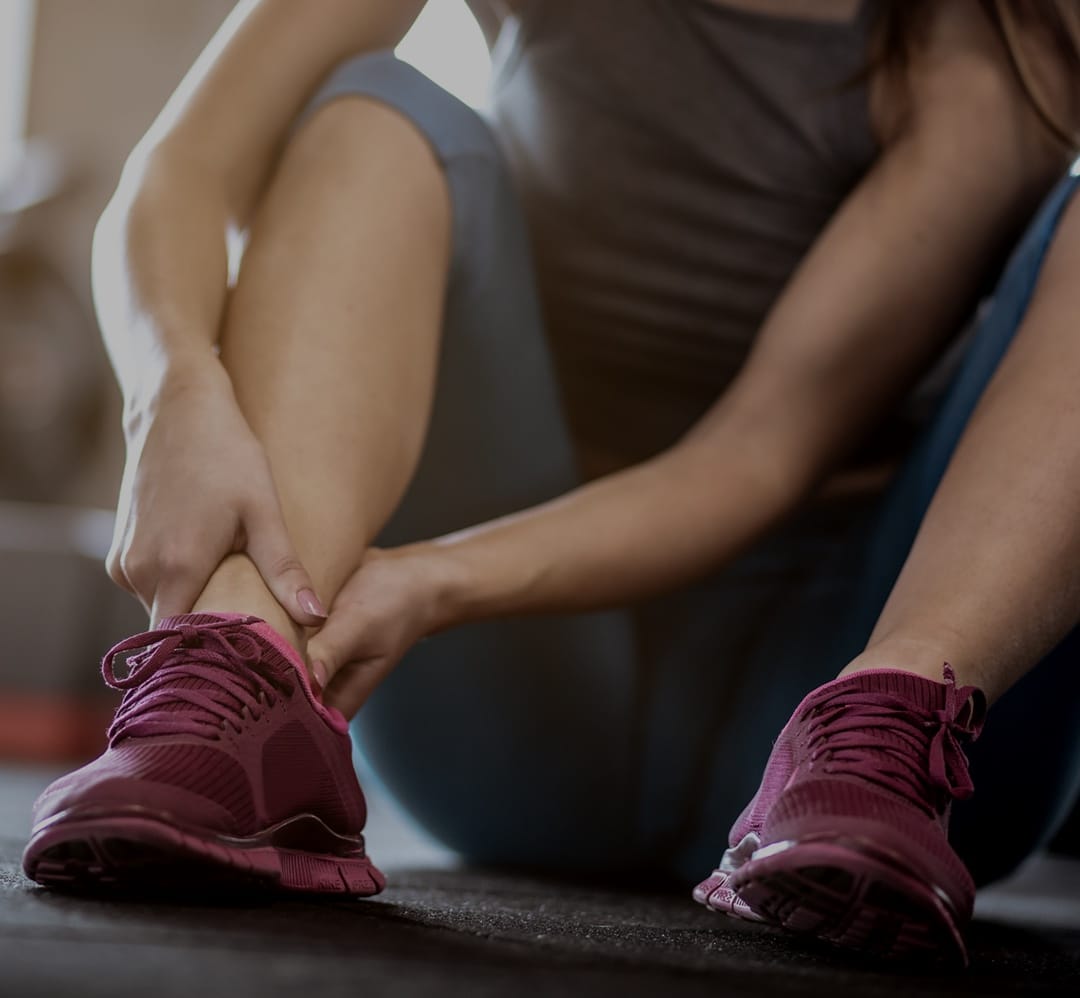Woman's back wearing black sports bra with hand on shoulder Person grabbing their ankle wearing red running shoes