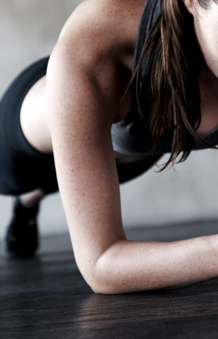 Woman's back wearing black sports bra with hand on shoulder Close of of the arm of a woman planking