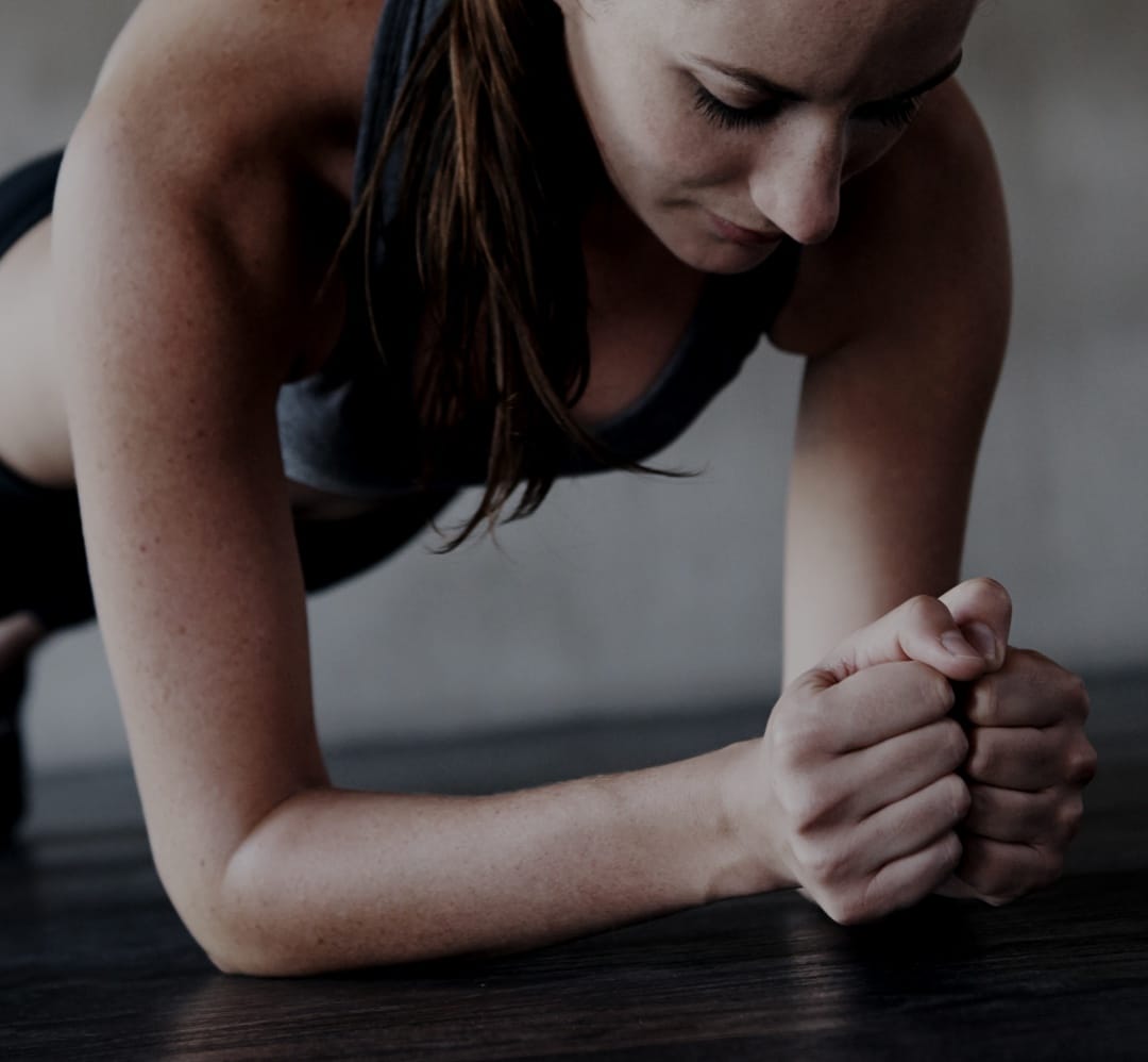 Woman's back wearing black sports bra with hand on shoulder Close of of the arm of a woman planking