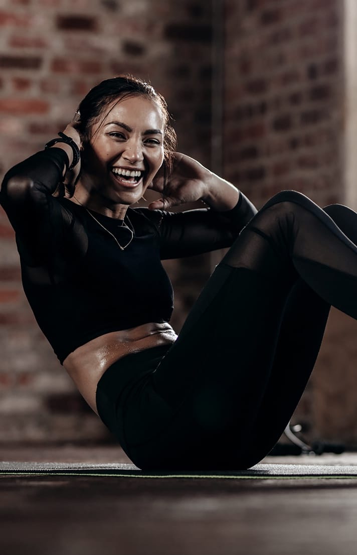 Woman's back wearing black sports bra with hand on shoulder Pretty woman wearing black workout outfit smiling while doing a situp