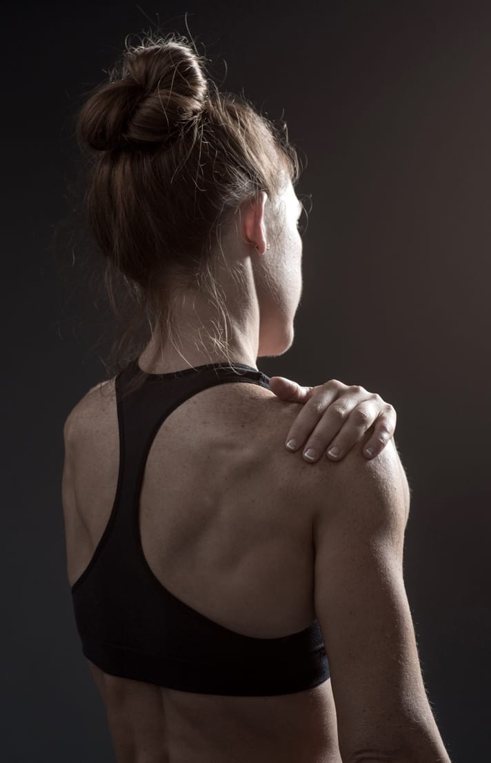 Woman's back wearing black sports bra with hand on shoulder Woman's back wearing black sports bra with hand on shoulder