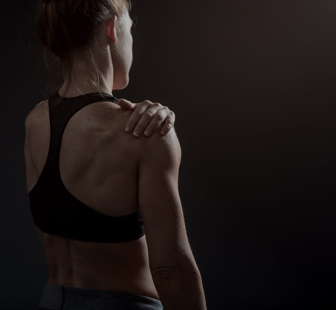 Woman's back wearing black sports bra with hand on shoulder Woman's back wearing black sports bra with hand on shoulder