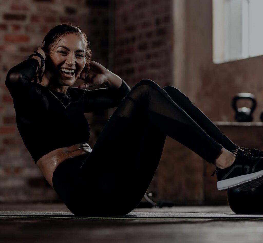 Pretty woman wearing black workout outfit smiling while doing a situp